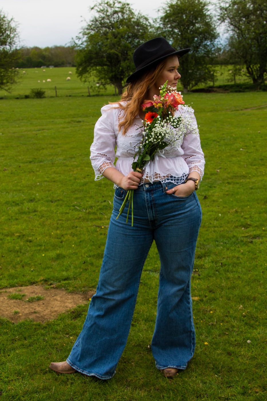 Hannah Collins in a field, hat on, bouquet in hand